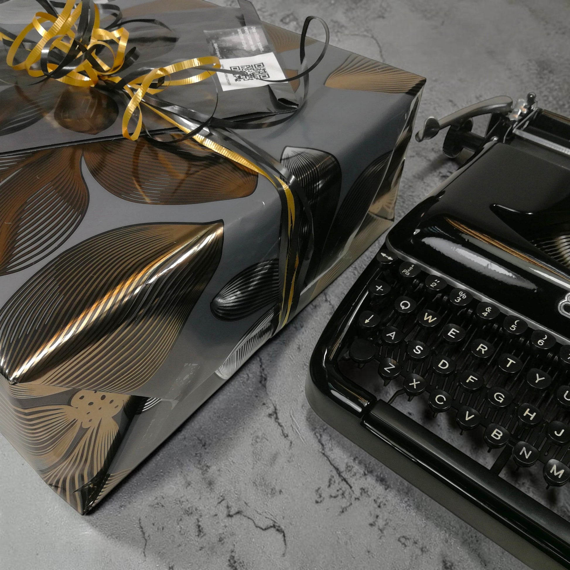 ElGranero Typewriter.Company premium gift wrap with black and gold floral paper, ribbon, and a vintage typewriter.