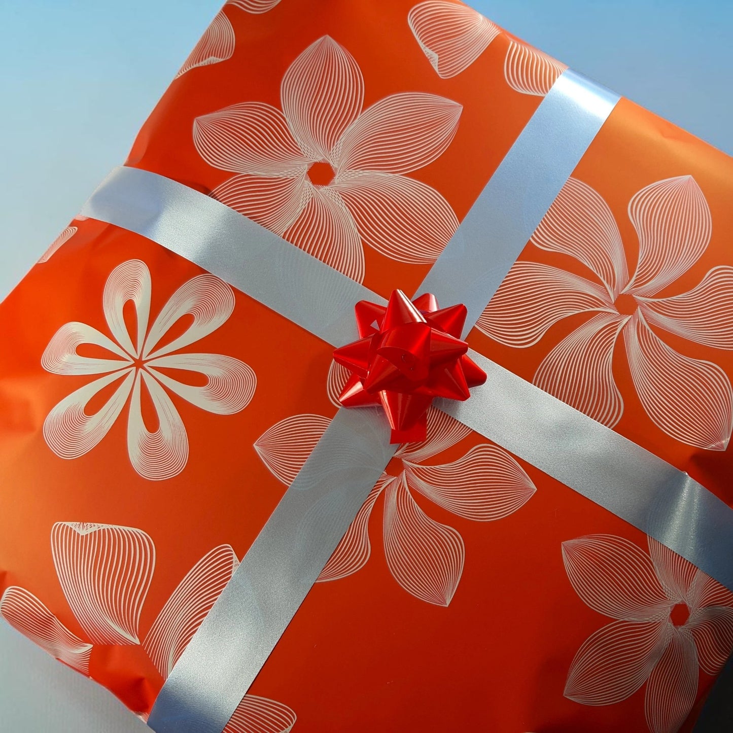 ElGranero Typewriter.Company premium gift wrap featuring orange paper with white floral patterns and a red bow.
